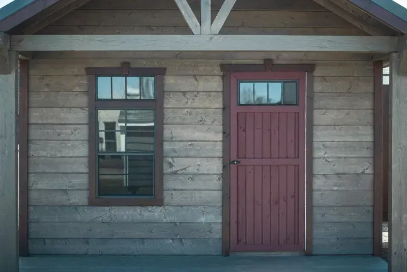 A wooden house with a red door and two windows