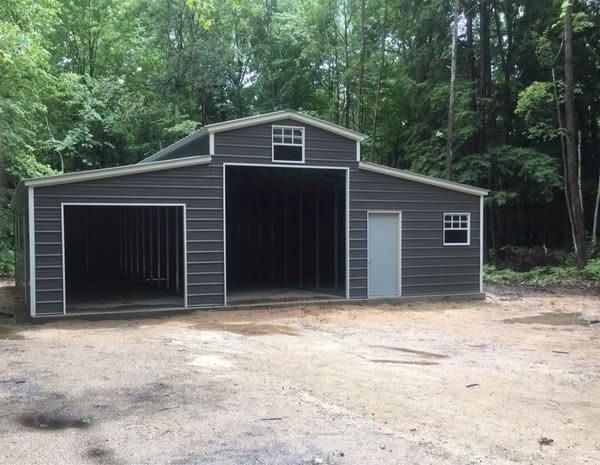 A large gray barn with a white door is sitting in the middle of a dirt field.