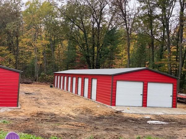 A red garage with white doors is sitting in the middle of a dirt field.