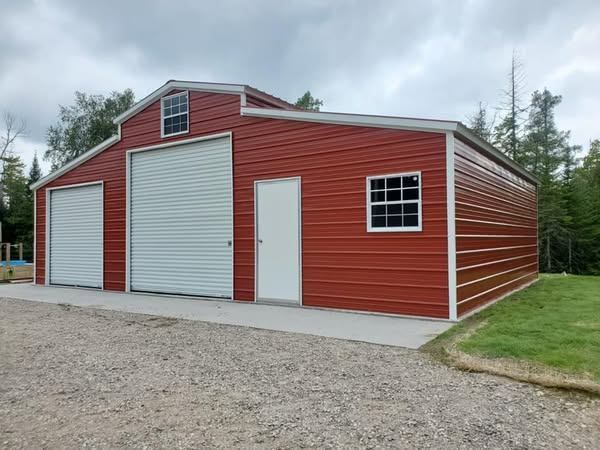 A red barn with white doors and windows is sitting on top of a gravel lot.