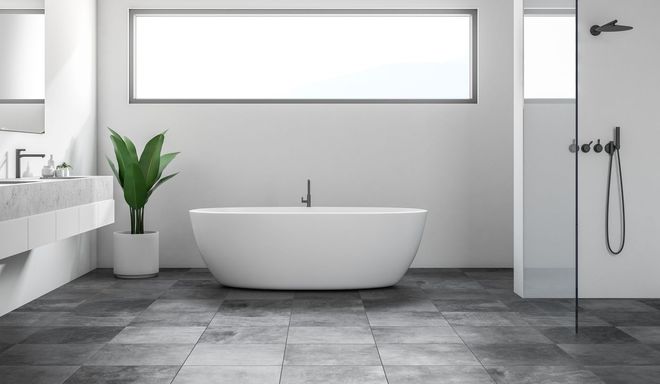 Modern gray bathroom with freestanding tub, large window, potted plant, and wall-mounted shower fixtures.