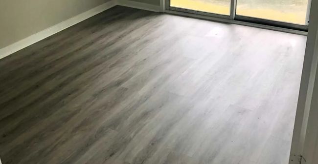 Empty room with gray wood-look flooring and large windows letting in natural light.