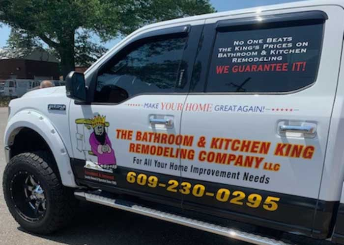 White contractor van with colorful “Bathroom & Kitchen King” remodeling company ads and phone number parked outdoors