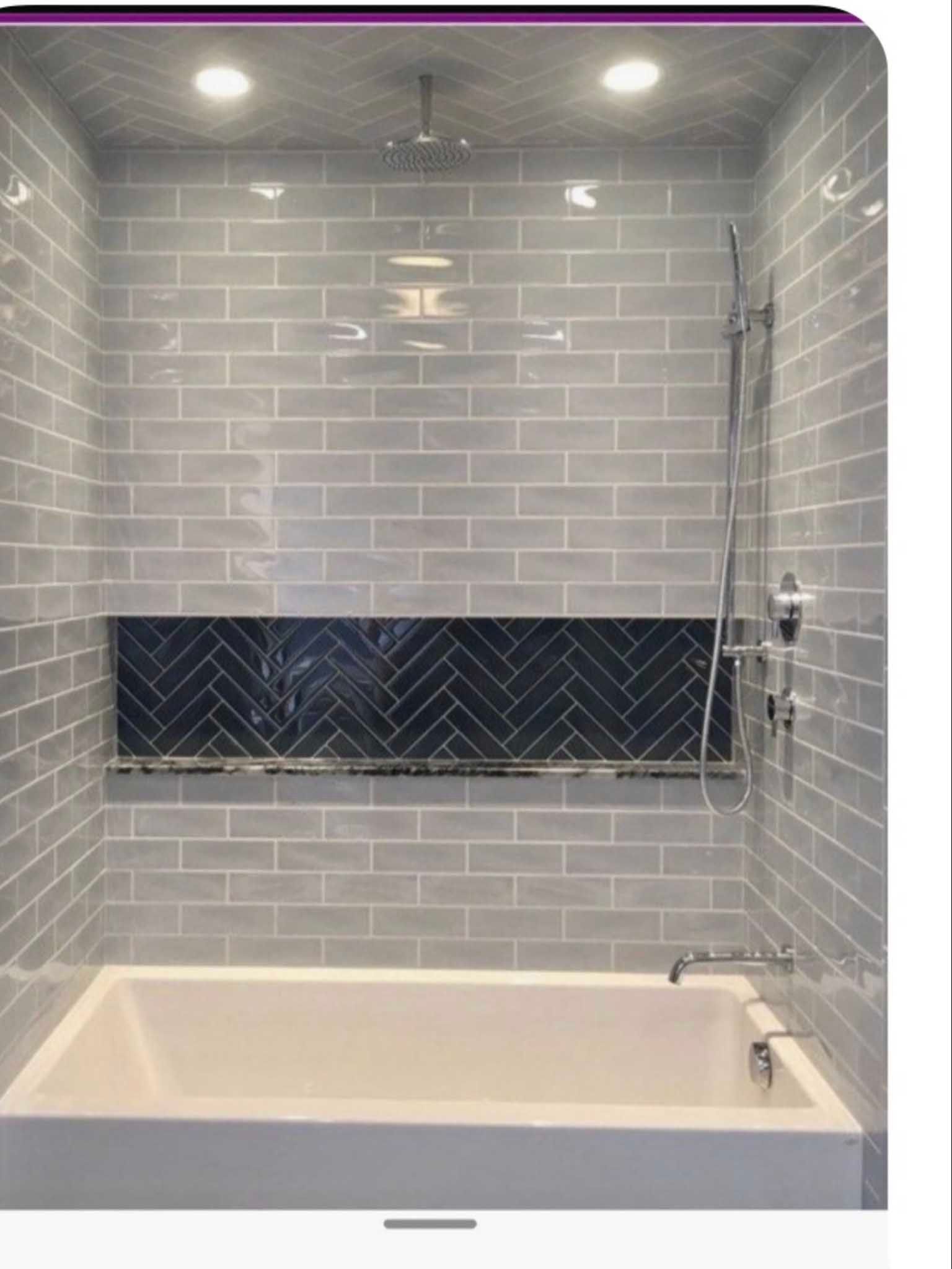 Modern tiled bathtub shower with gray subway tiles, dark accent band, glass partition, and built-in shelf.