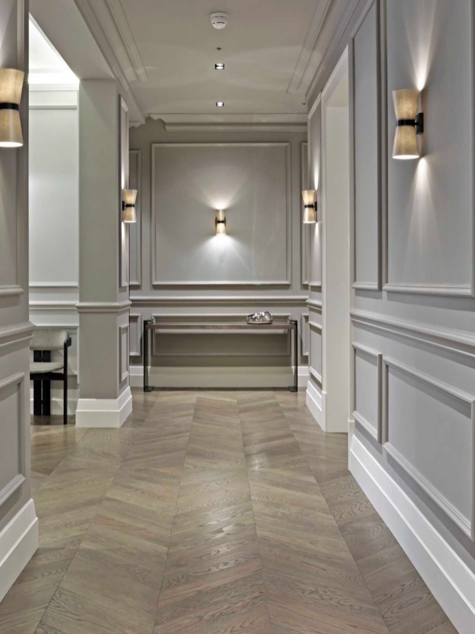 Elegant hallway with gray paneled walls, wall sconces, and herringbone wood flooring