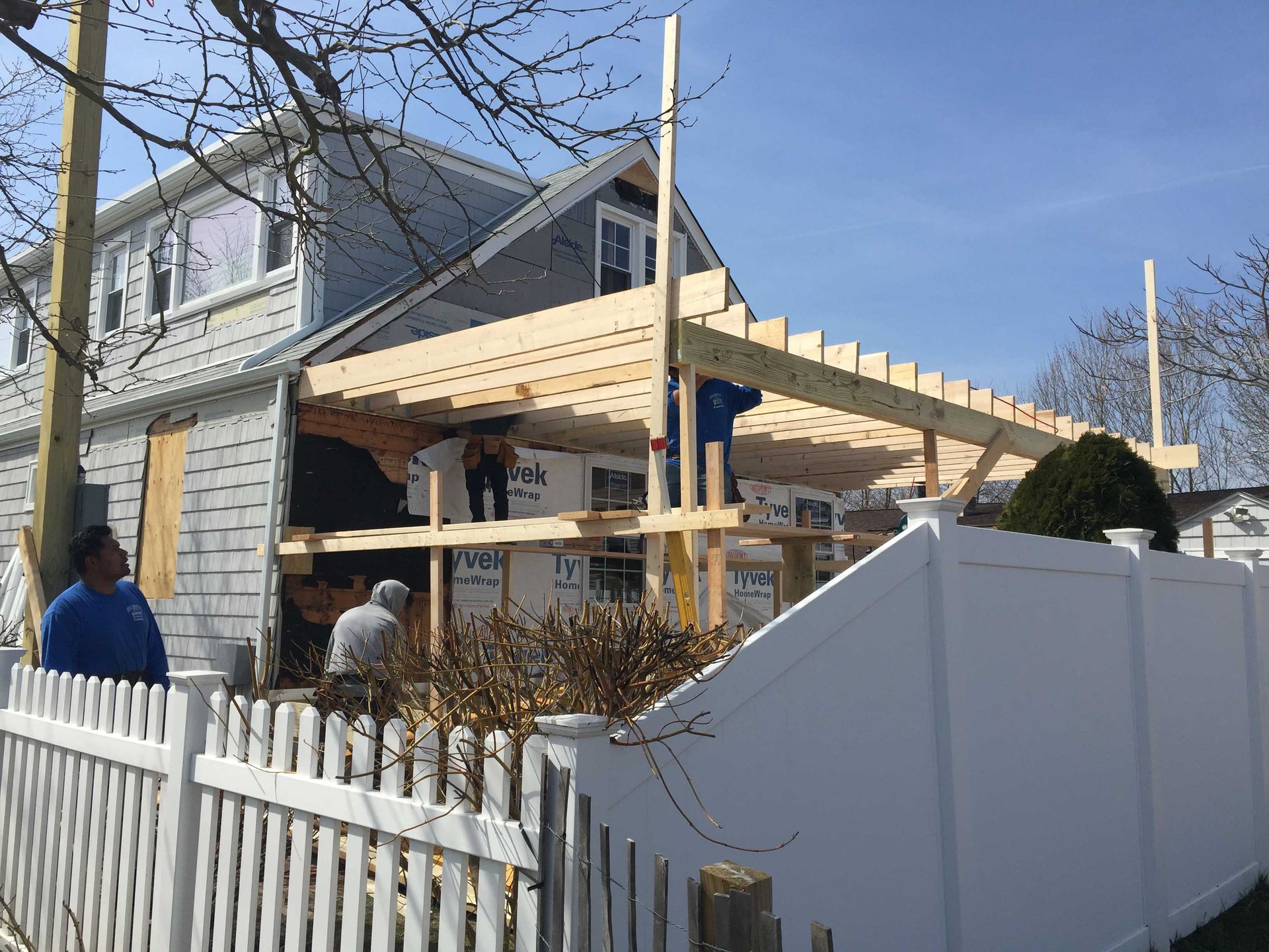 Residential house with a new wooden porch frame under construction behind a white fence
