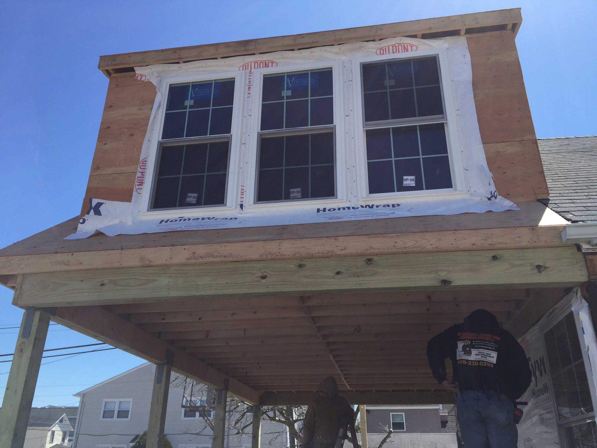 House under construction with white-trimmed windows and a worker on scaffolding below.