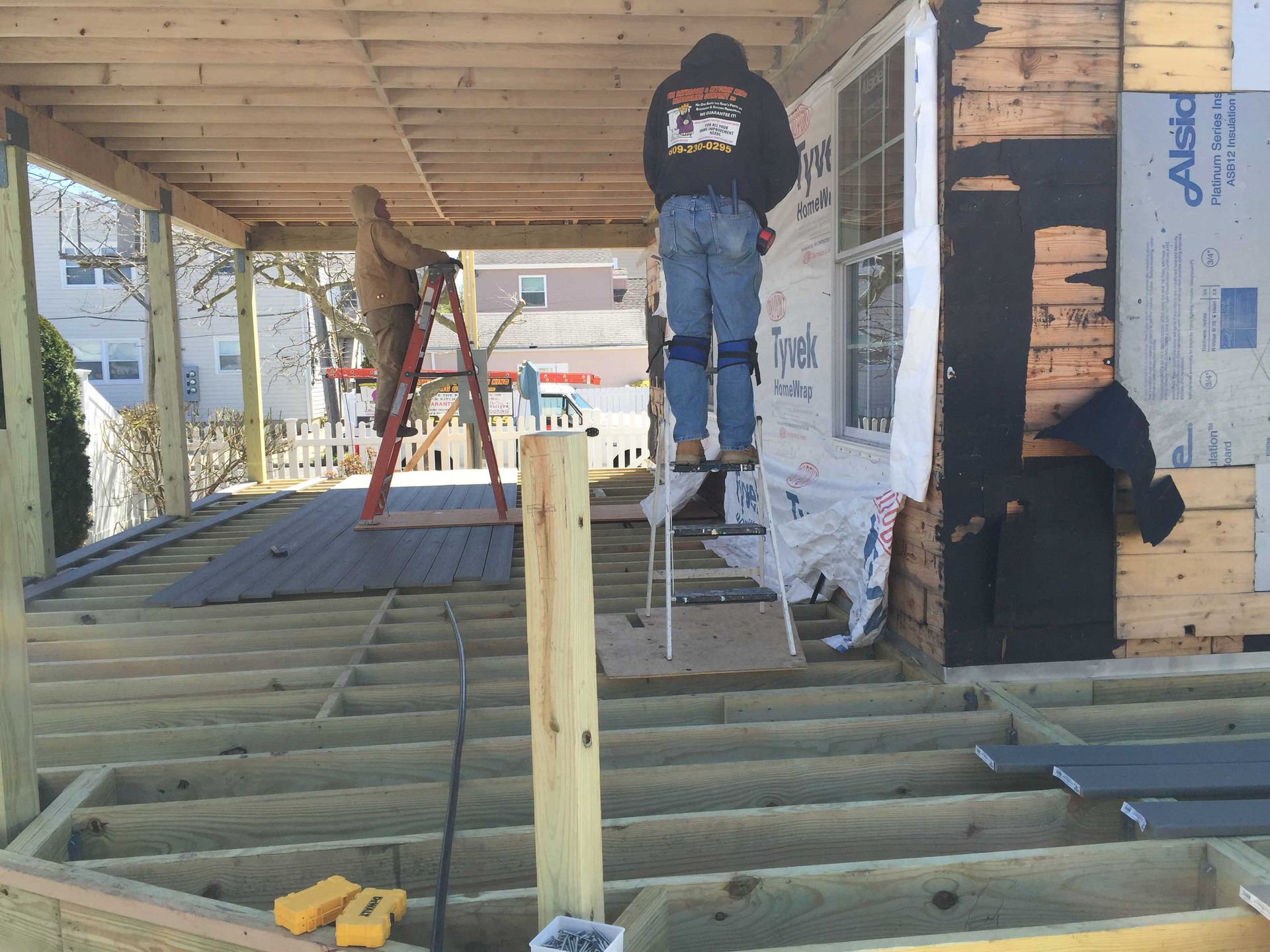 Workers installing a porch deck frame on a house under construction, with insulation and tools visible