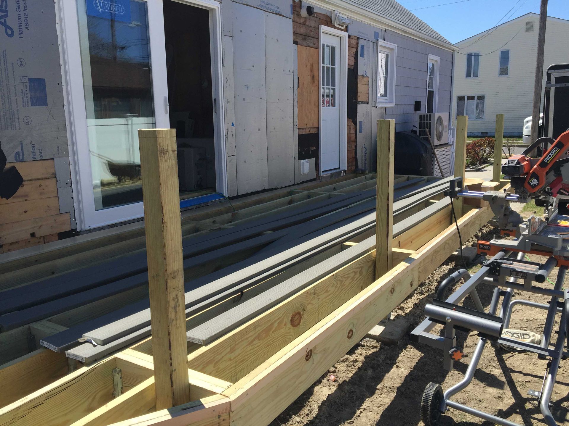Wooden framing under construction beside a row of houses on a sunny day
