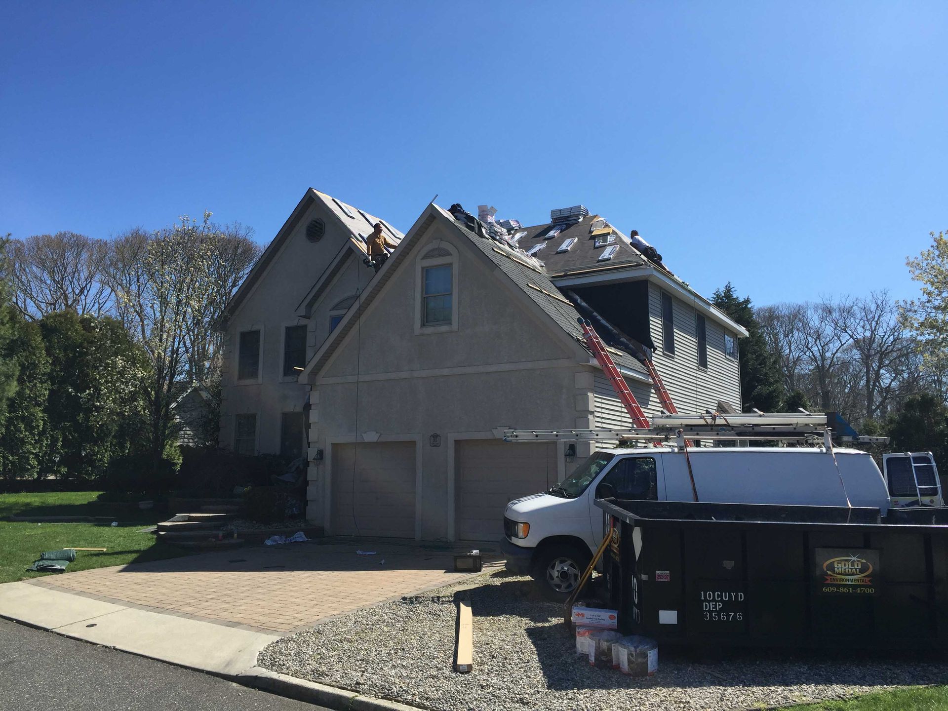 Damaged house with roof collapse, white truck, and debris in driveway under clear blue sky