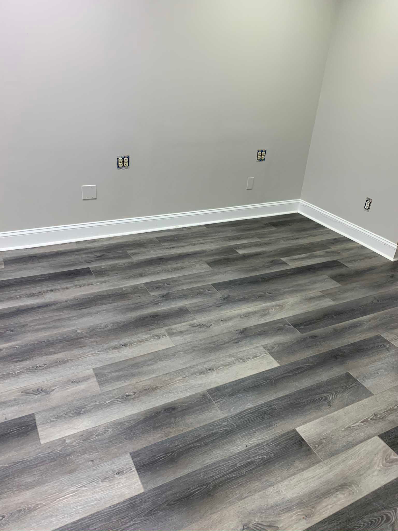Empty room with gray walls, white baseboards, and dark gray wood-look flooring.