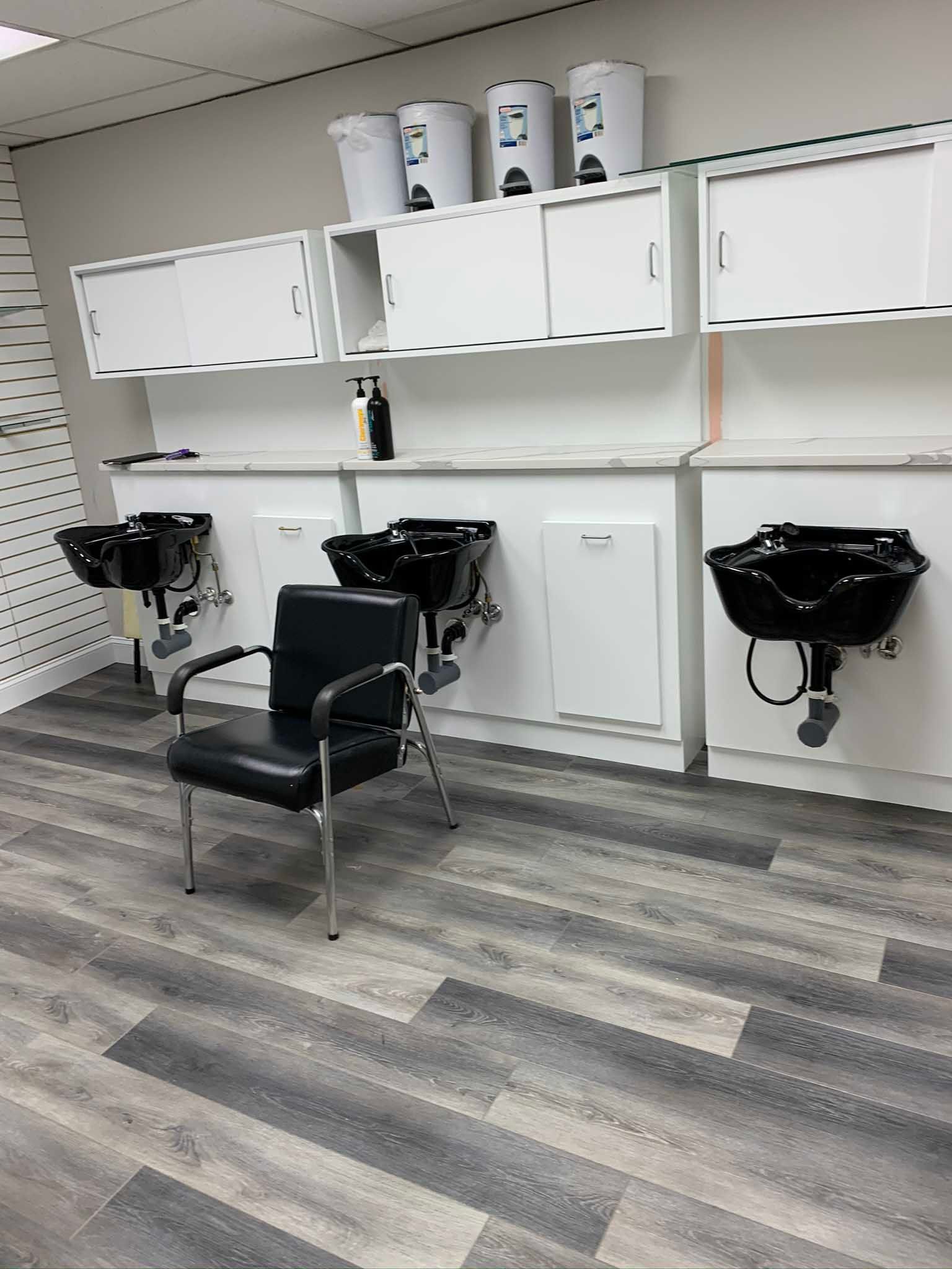 Salon wash station with black shampoo sinks, white cabinets, and a black chair on a gray wood floor.