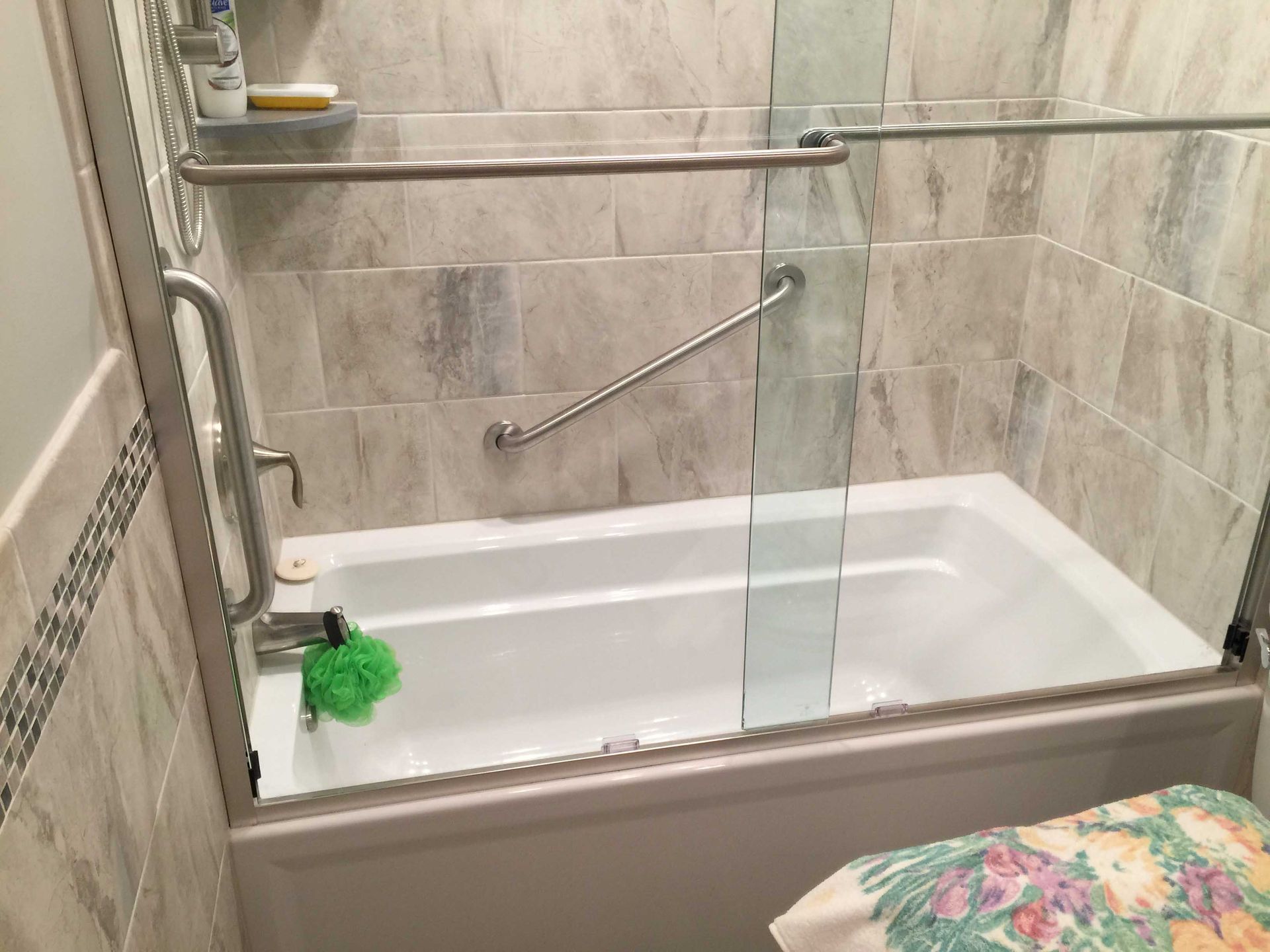 Bathroom with a white bathtub, glass shower panel, grab bars, and beige tile walls