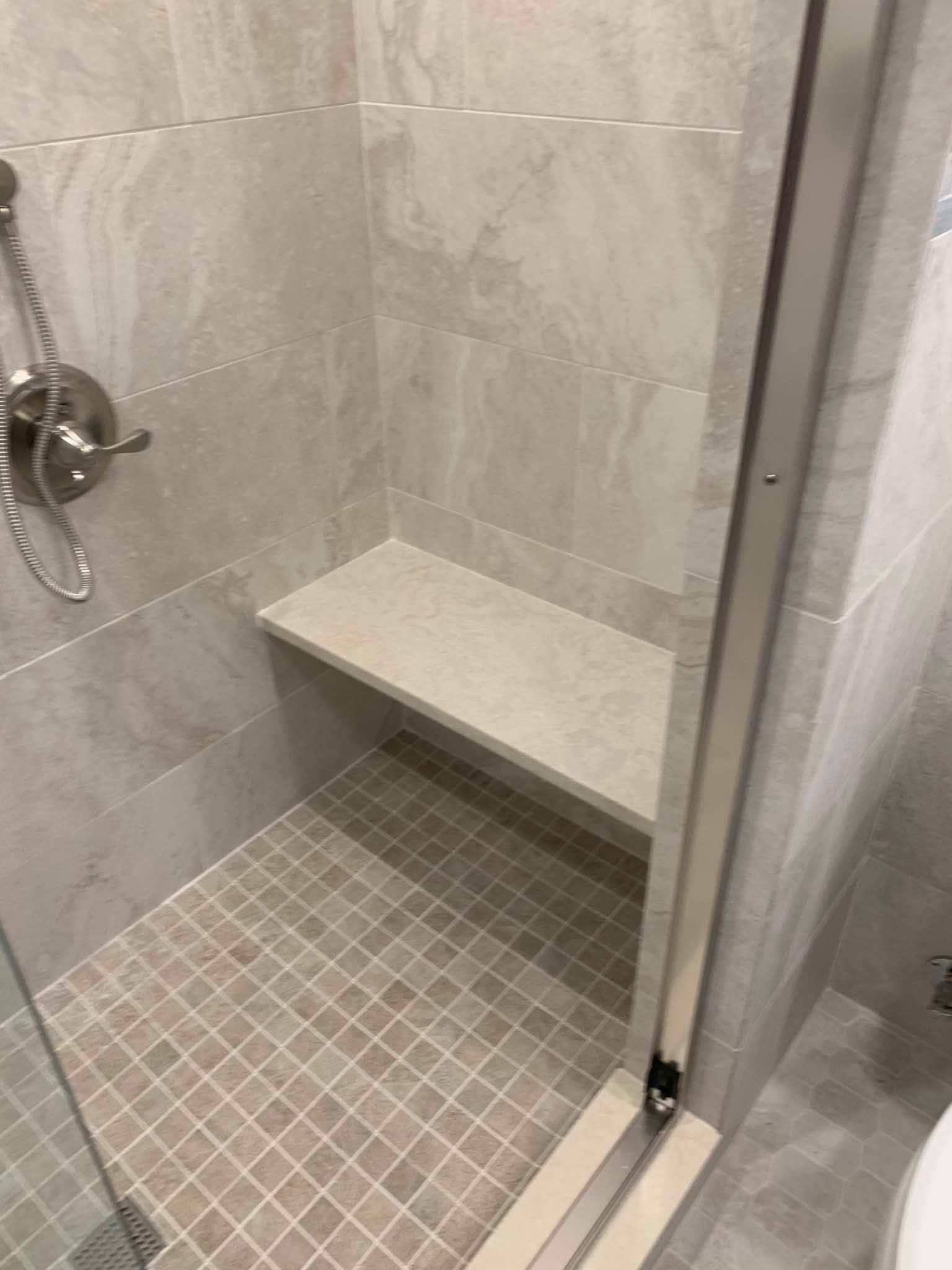 Small tiled shower stall with a built-in bench and chrome showerhead.