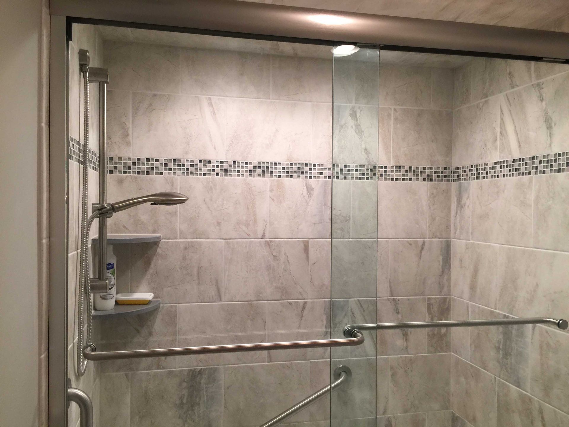 Tiled shower with glass enclosure, chrome grab bars, and built-in corner shelves.