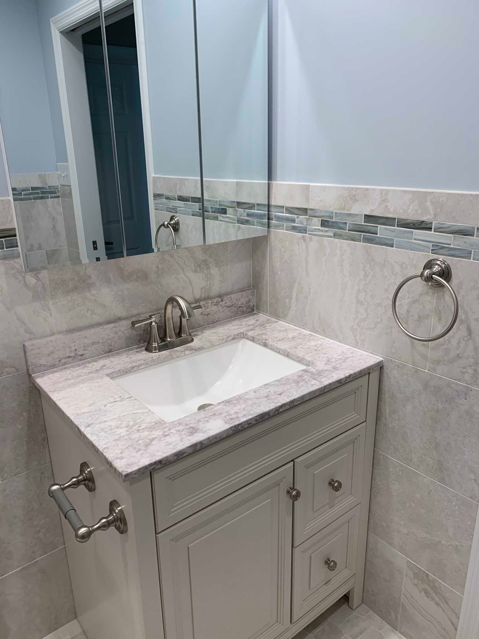Small bathroom vanity with white sink, marble countertop, mirror, and chrome towel ring.