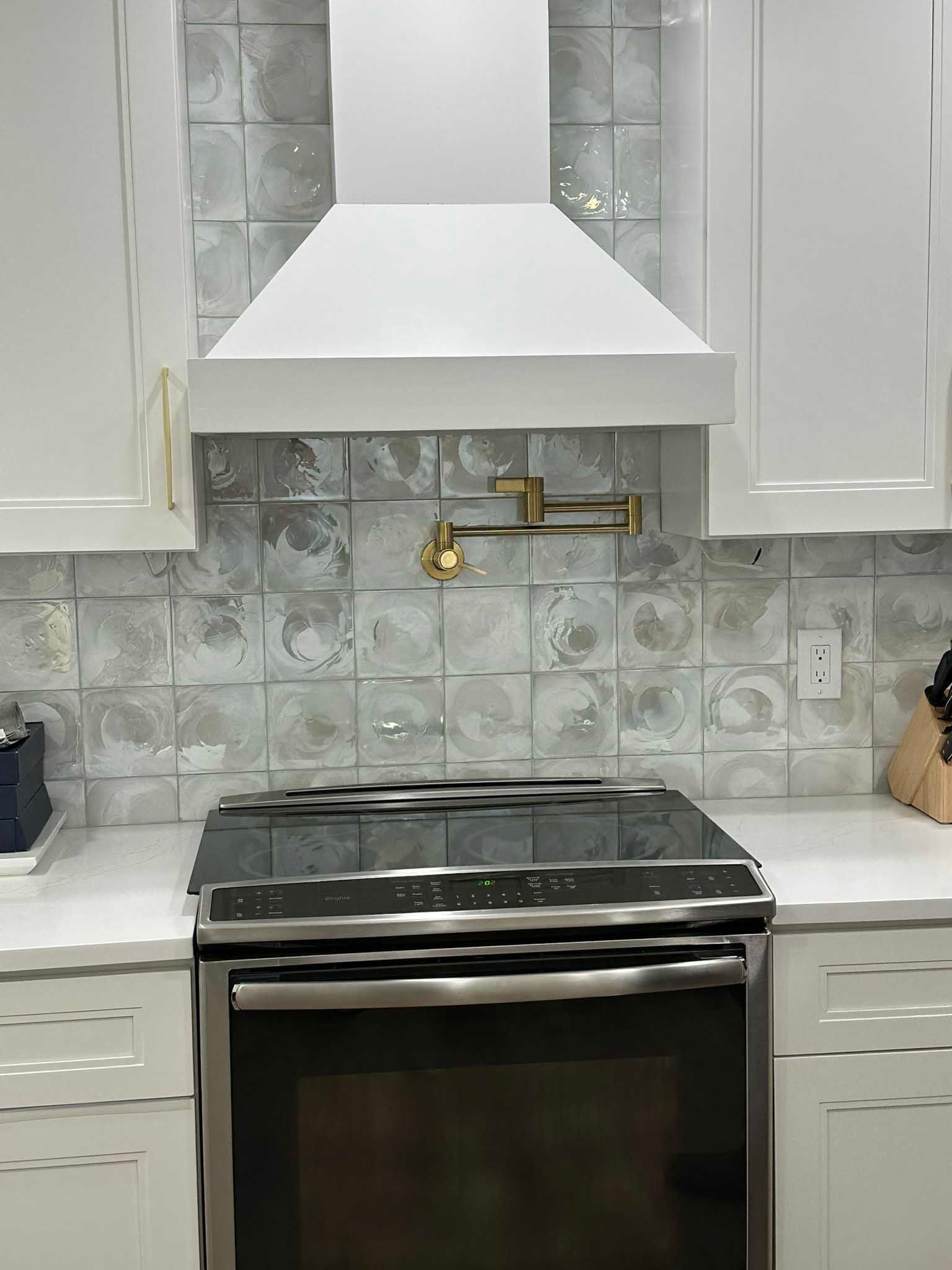 Modern kitchen with white cabinets, stainless stove, and white range hood against a gray tile backsplash