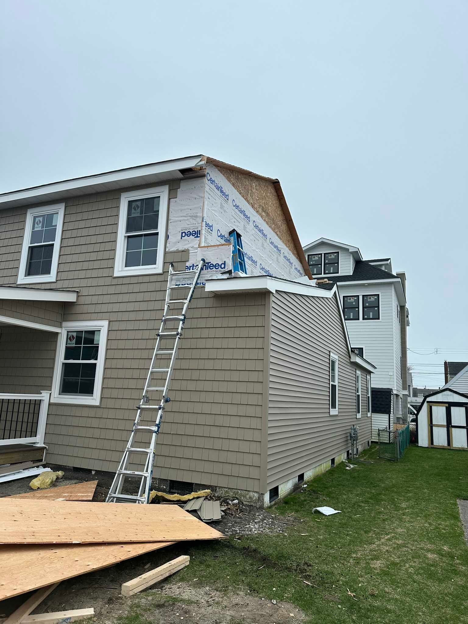 House exterior under renovation with ladder, siding work, and construction materials on the ground