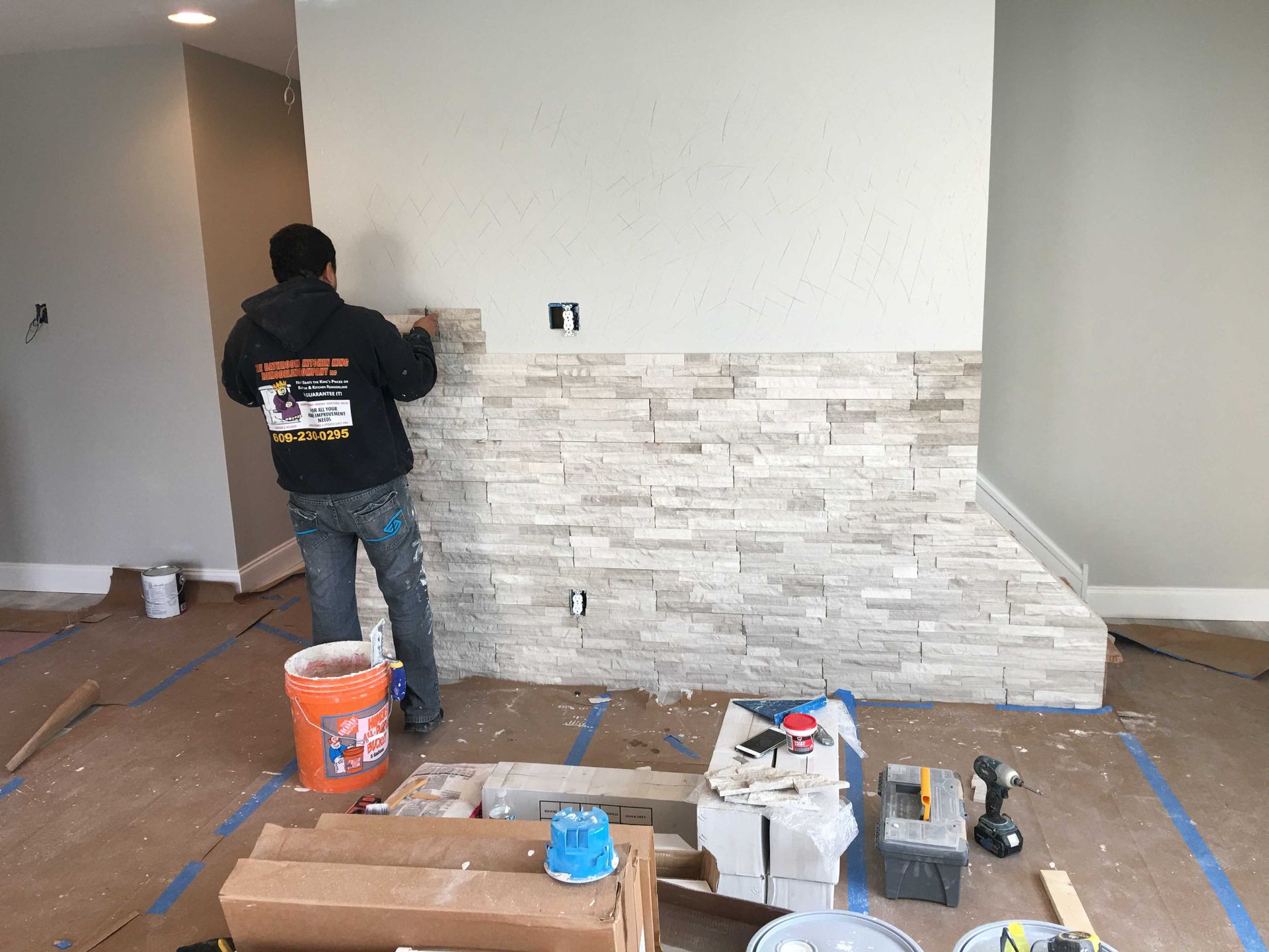 Worker installing white stacked-stone wall paneling in a room with tools and supplies on the floor