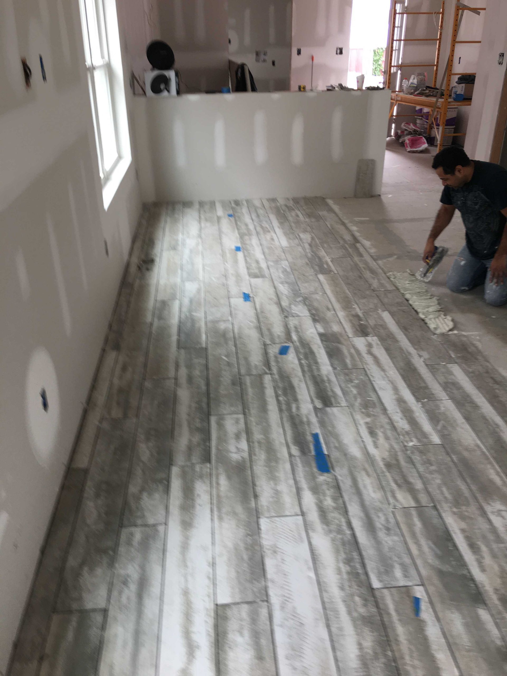 Partially finished room with wood-look flooring; worker kneels on the right near a white wall.