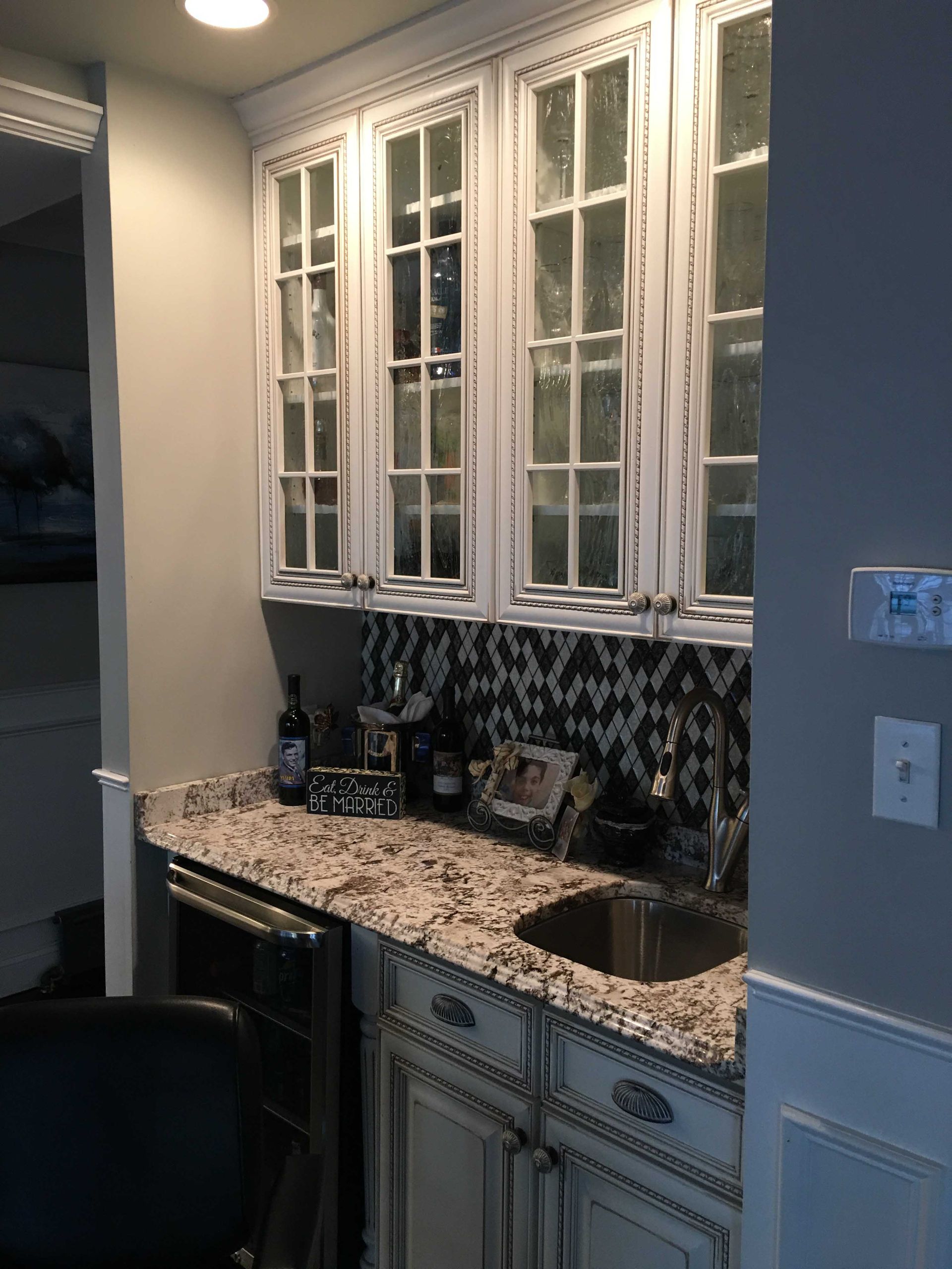 Small bathroom vanity with granite countertop, sink, mirror cabinets, and patterned tile backsplash.