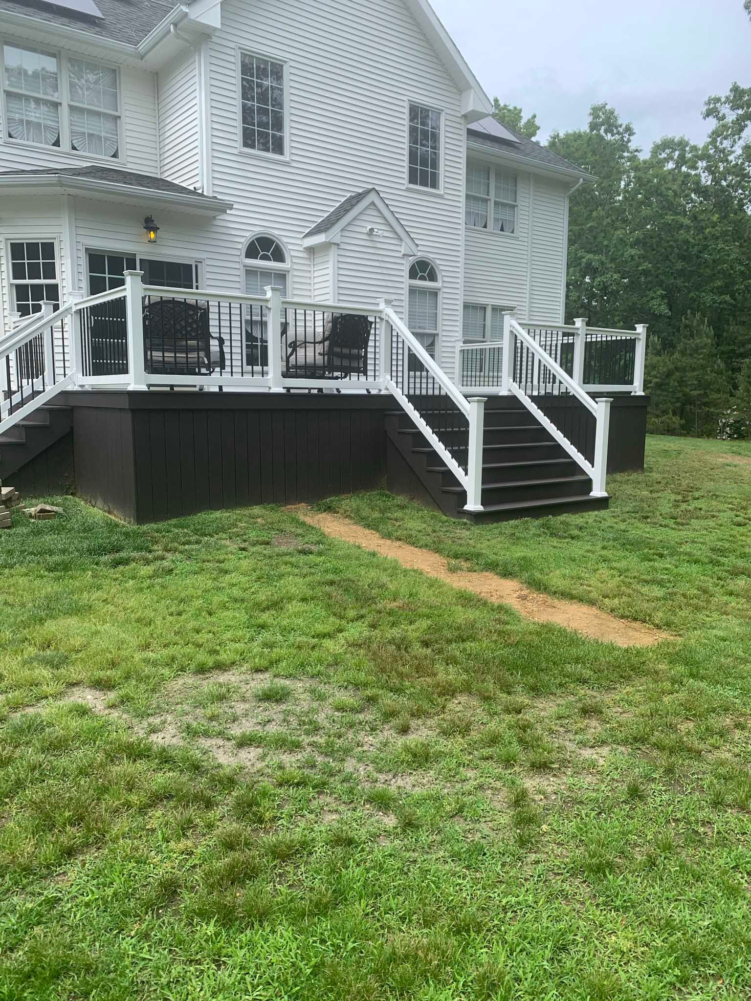 White house with dark deck and stairs in a grassy yard, viewed from the side.