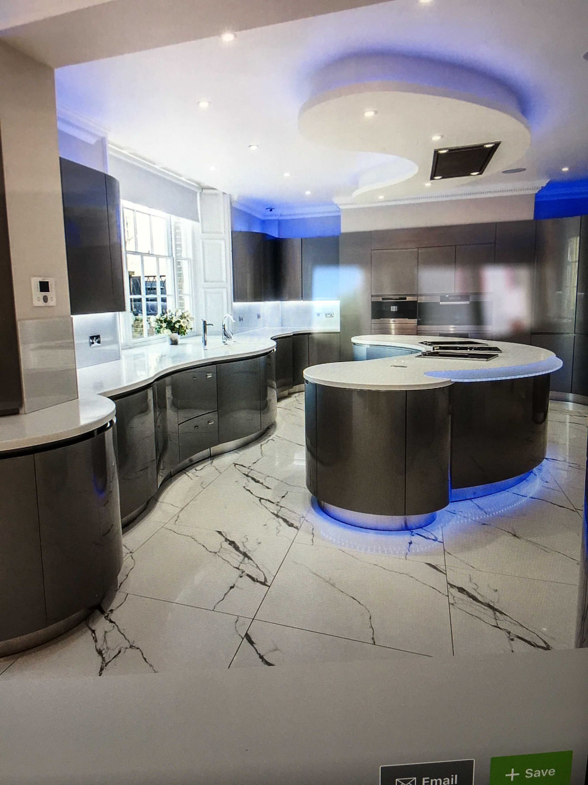 Modern kitchen with curved black island, blue underlighting, white cabinets, and tiled floor