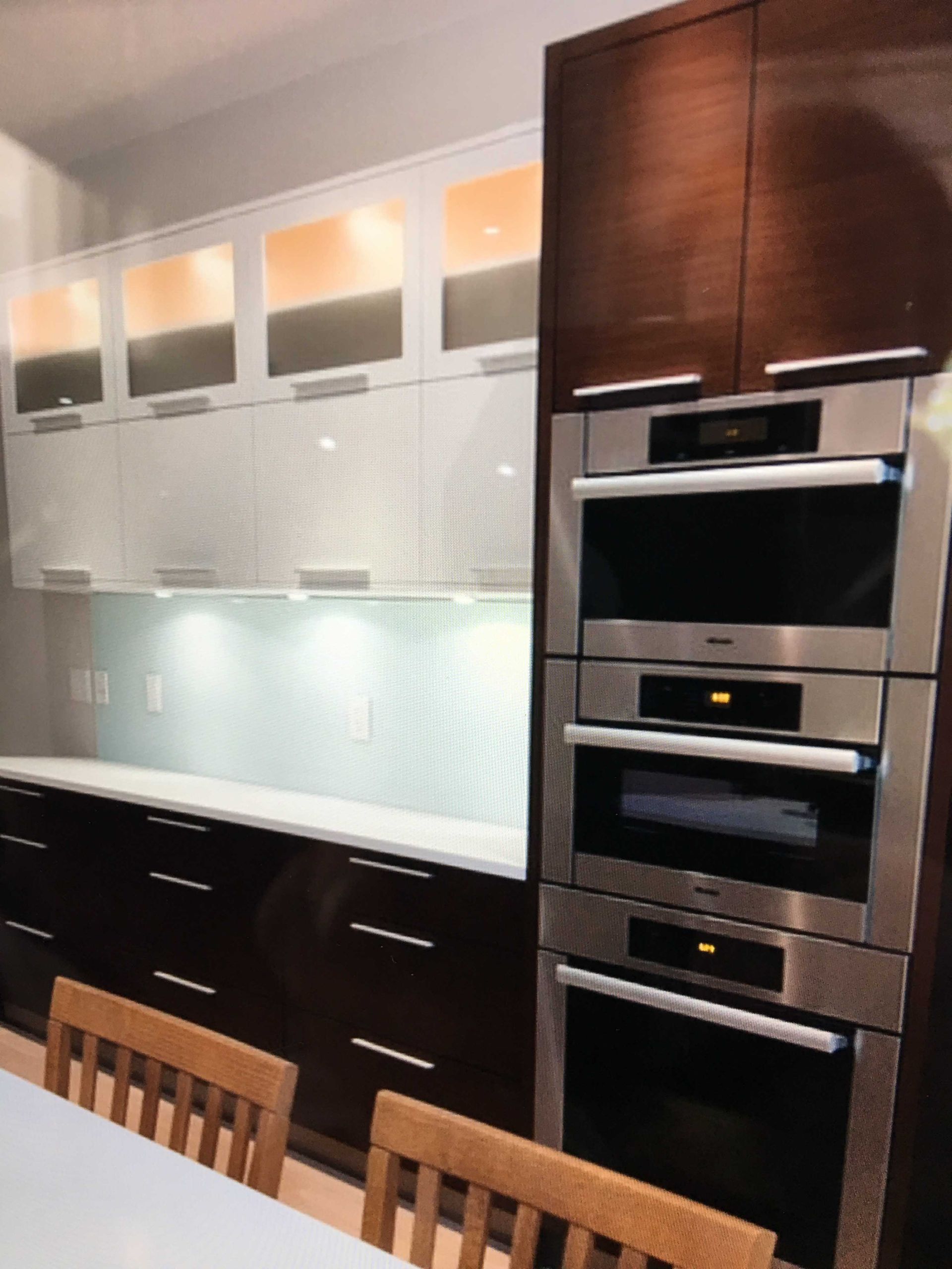 Modern kitchen with dark wood cabinets, built-in ovens, frosted glass uppers, and black countertops.