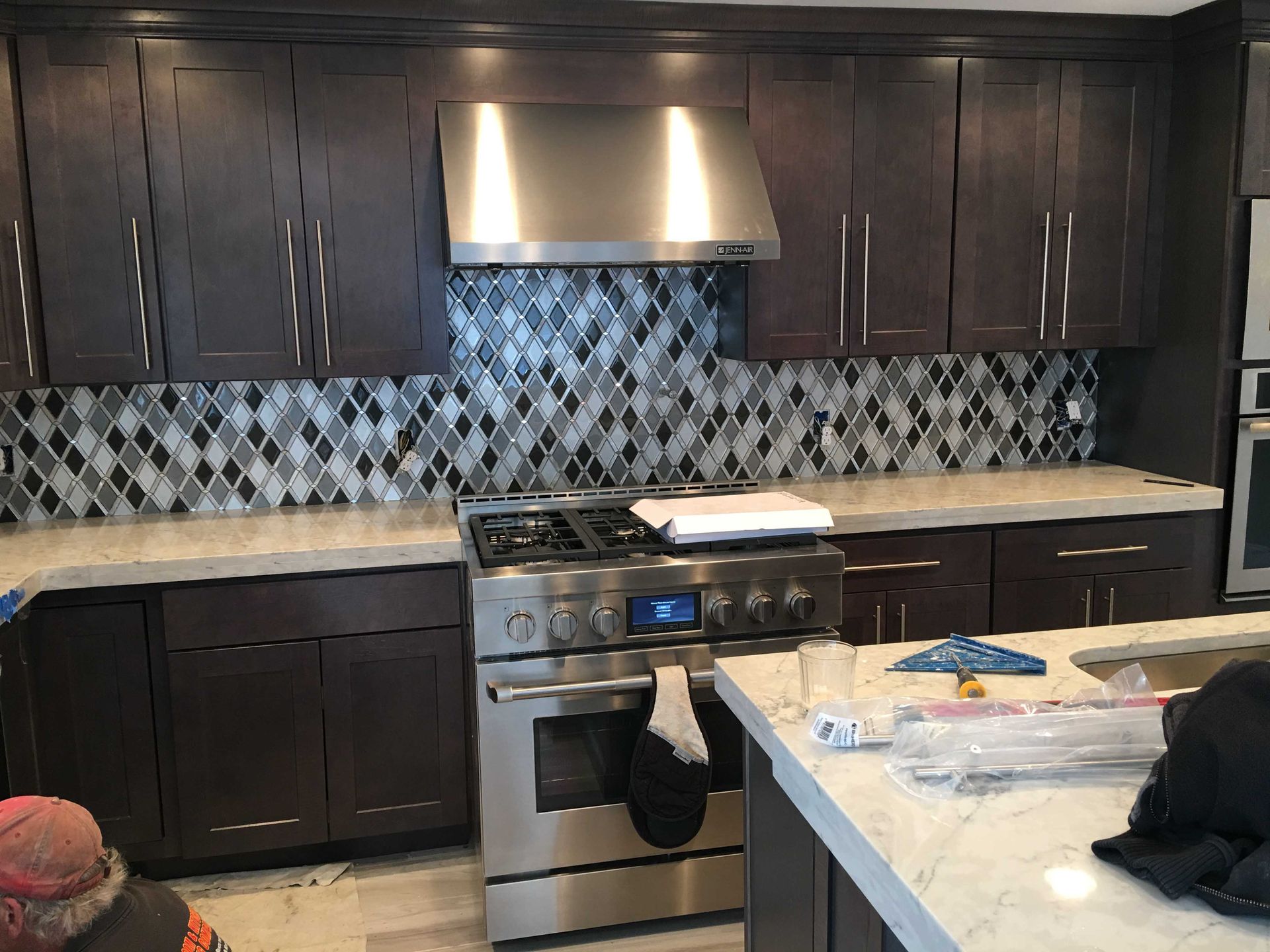 Modern kitchen with dark cabinets, stainless stove hood, blue-patterned backsplash, and a countertop island in front