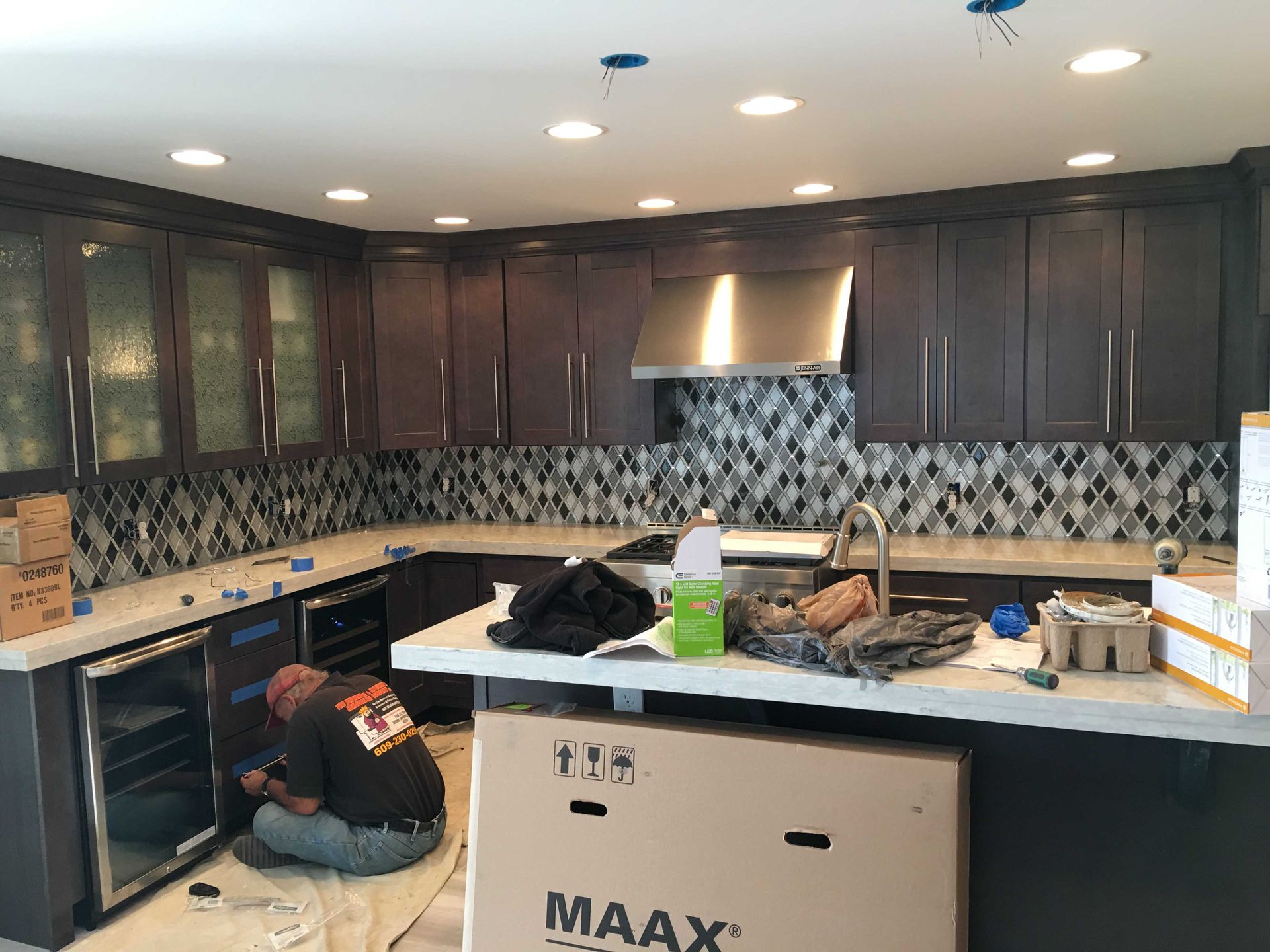 Kitchen under renovation with dark cabinets, backsplash tile, and contractors working on the floor.