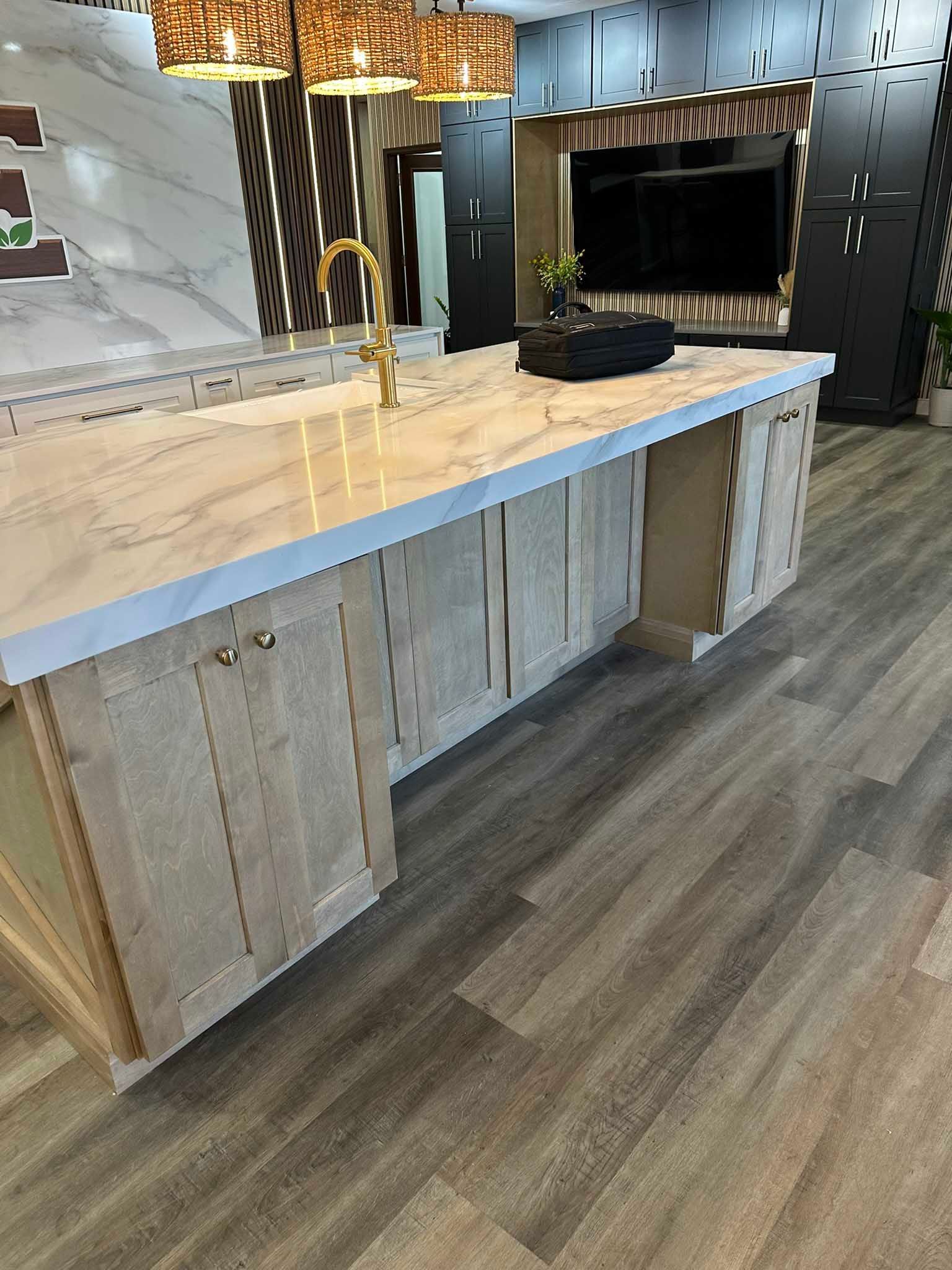 Modern kitchen island with light wood cabinets, white marble countertop, and gold faucet.