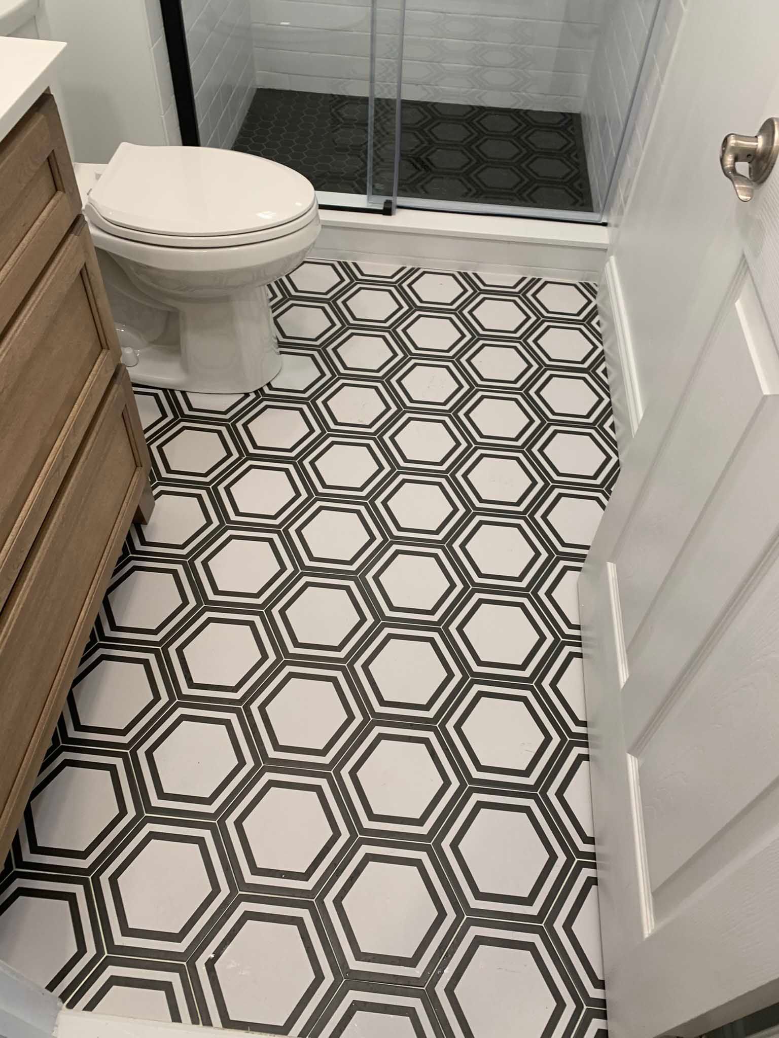 Small bathroom with black-and-white hexagon floor tiles, toilet, vanity, and glass shower door.