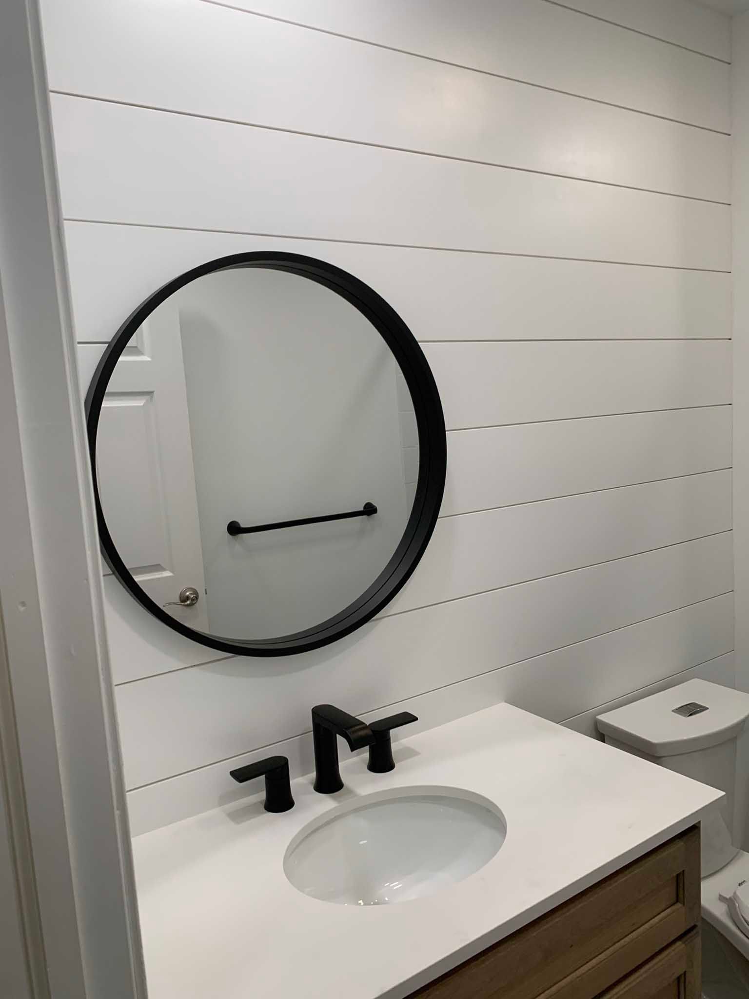 Modern bathroom vanity with round black mirror, white sink, and black faucet on shiplap wall