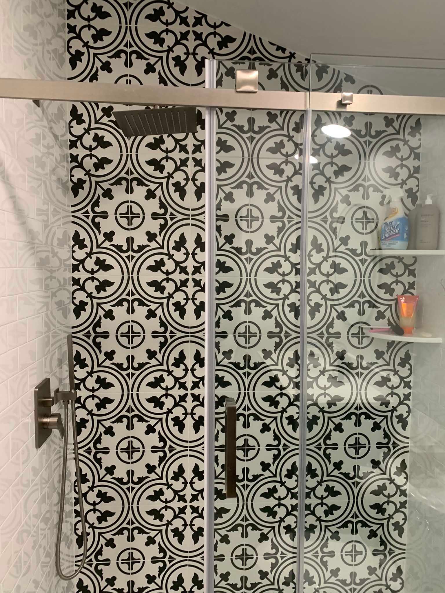 Patterned glass shower enclosure with black-and-white decorative tiles and a shelf on the right