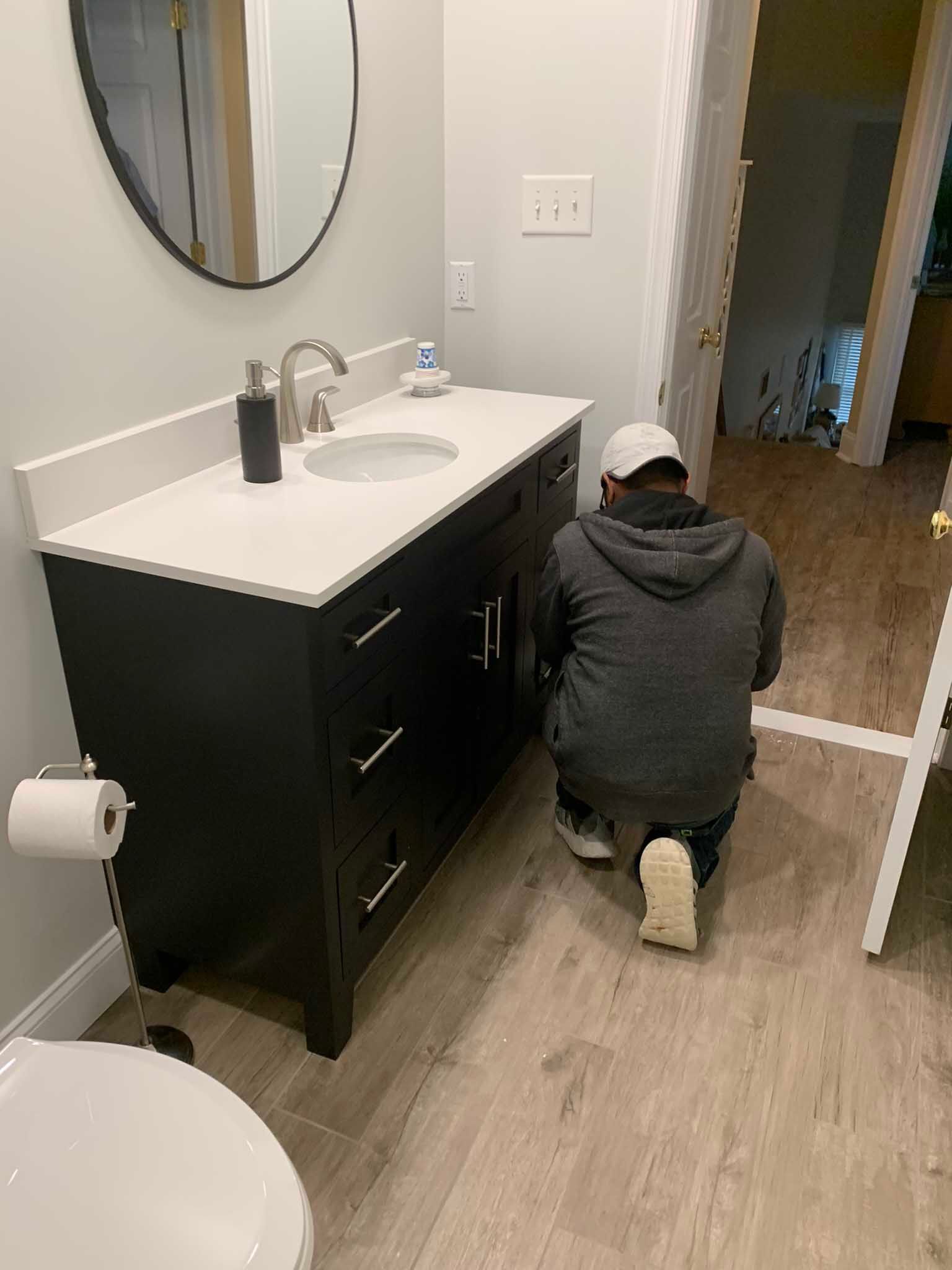 Person kneeling on a bathroom floor beside a dark vanity and sink, working near the doorway.