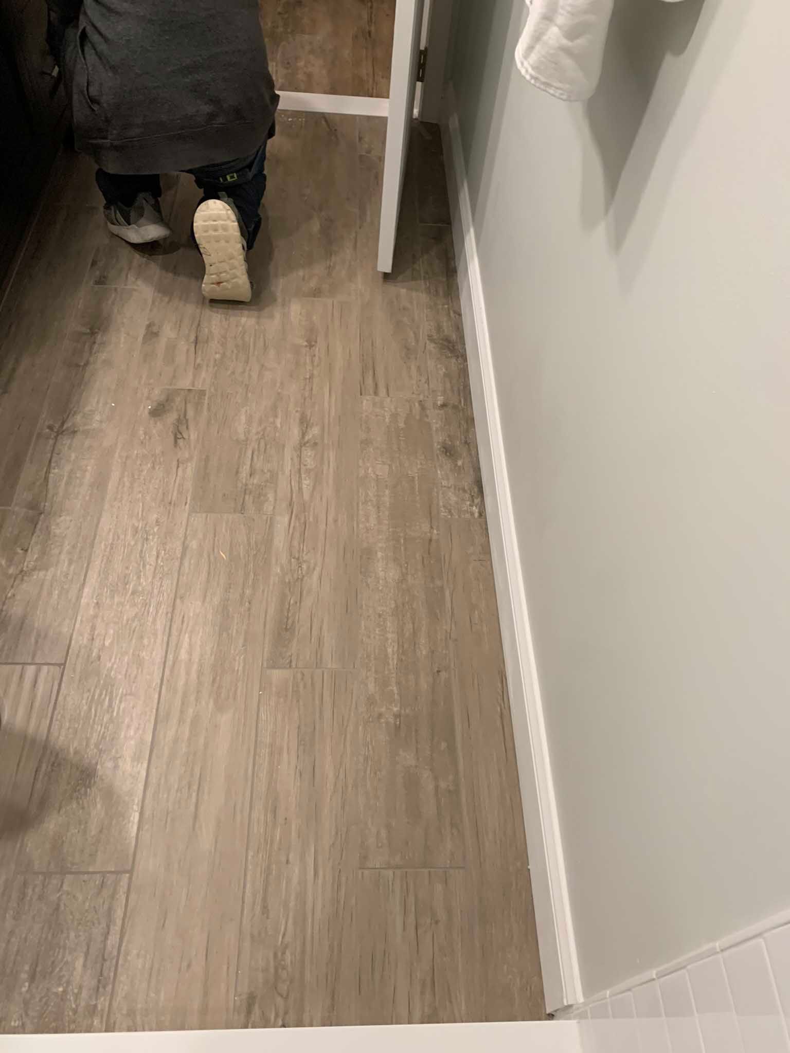 Person walking through a narrow hallway with wood flooring and white walls