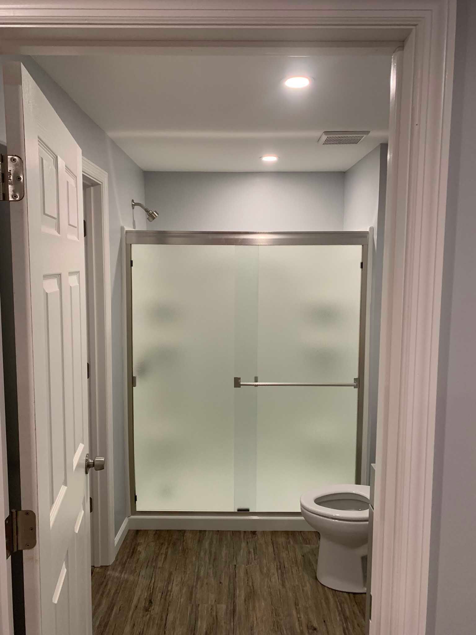 Hallway view into a bathroom with frosted glass shower doors and a toilet on the right.