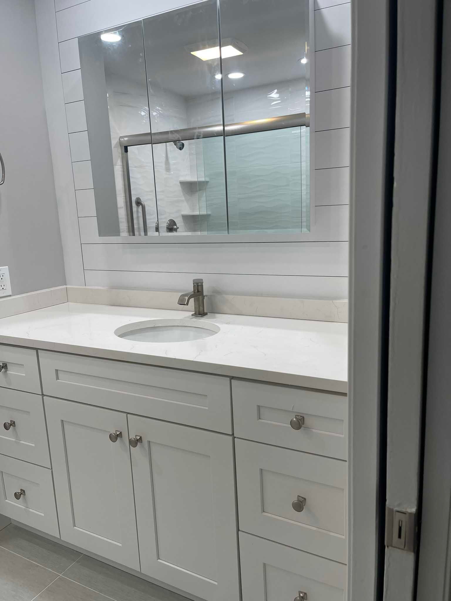 White bathroom vanity with sink, mirror, and built-in lighting, seen through a doorway.
