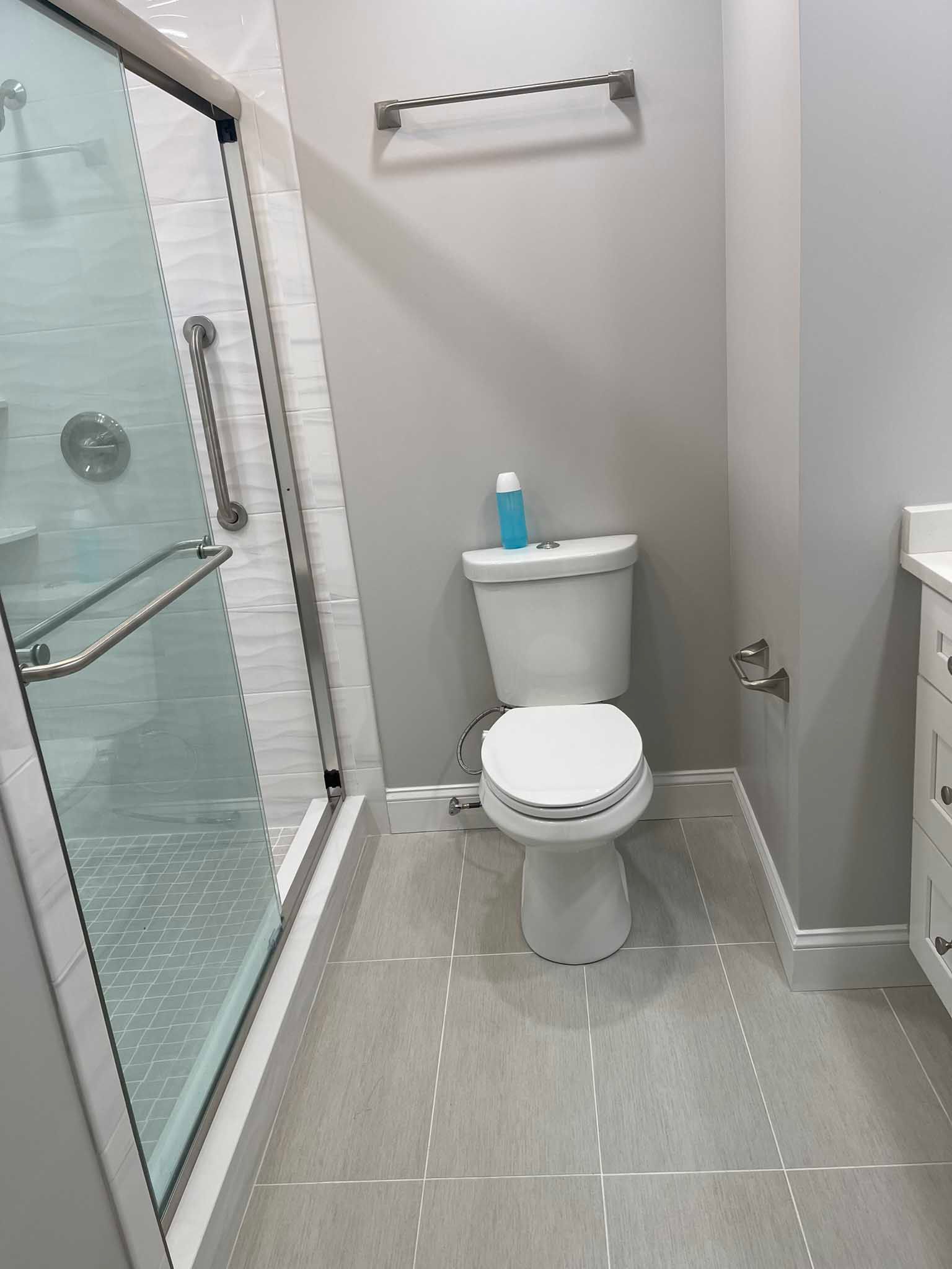 Small bathroom with toilet, shower stall, and towel bar, in gray and white tones.