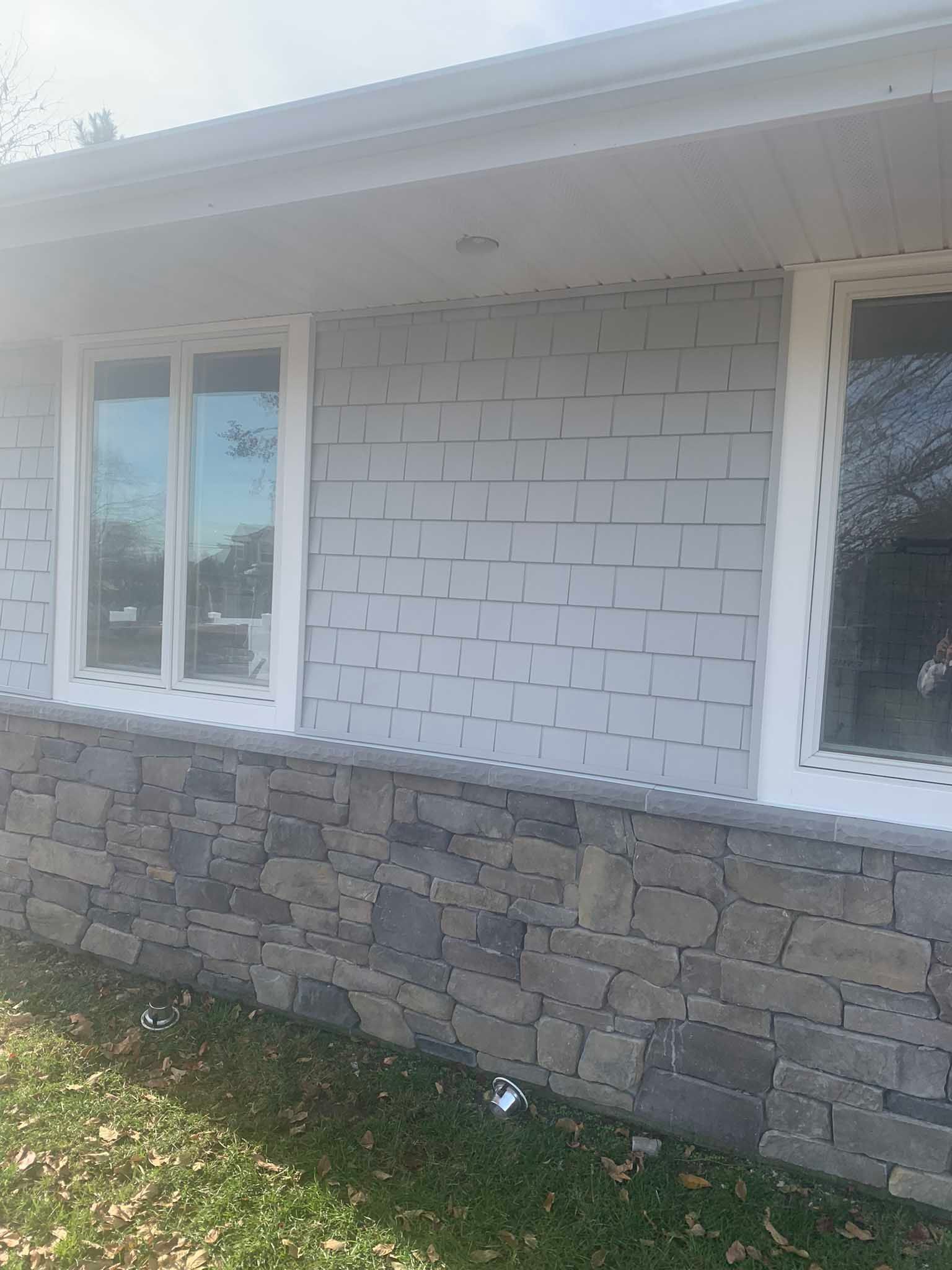 Exterior of a white house wall with windows and stone foundation under the eaves