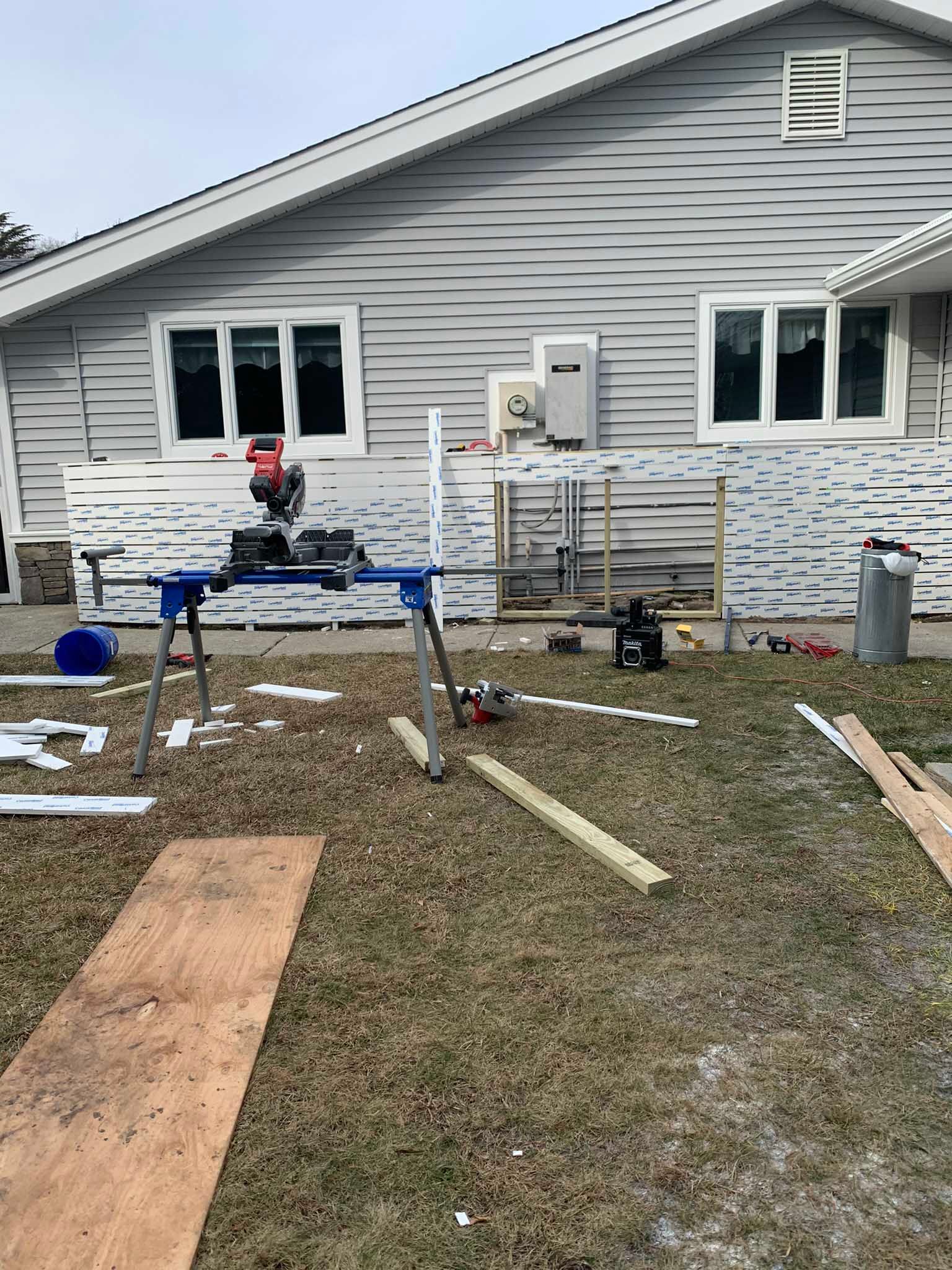 House exterior under construction with siding, windows, and scattered tools and lumber in the yard