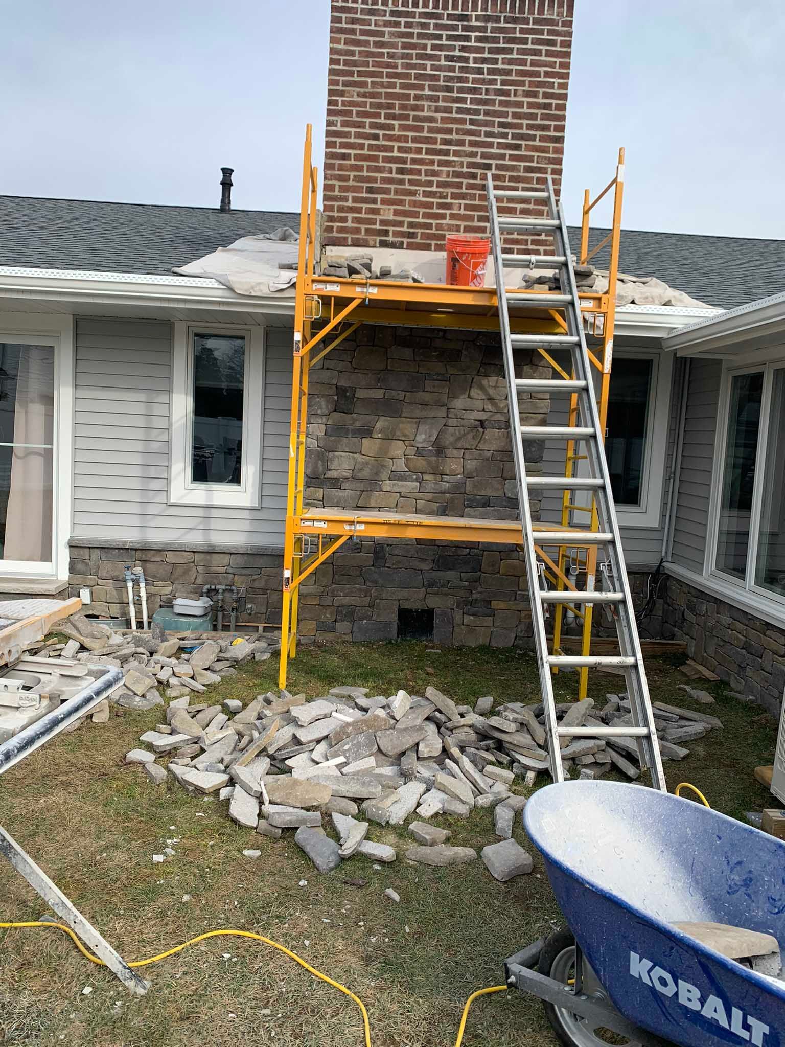 House exterior with scaffold and ladder around a brick chimney during masonry repair