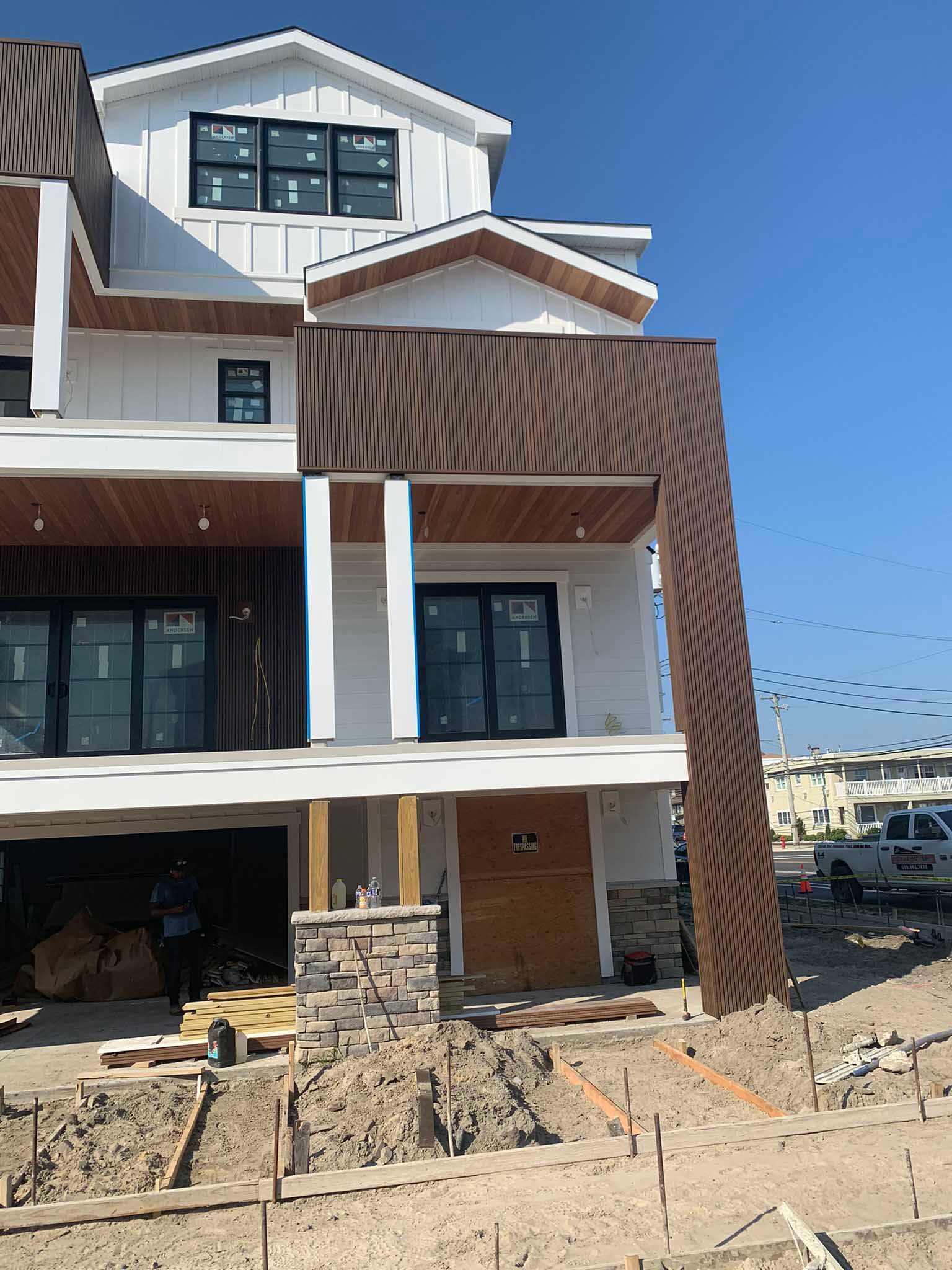 Modern townhouse under construction with white siding, brown wood accents, and stone facade.