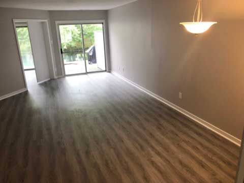 Empty living room with gray wood floors, beige walls, and sliding glass doors to a balcony.