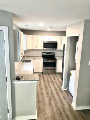 Bright kitchen with white cabinets, gray countertops, black appliances, and wood-look flooring.