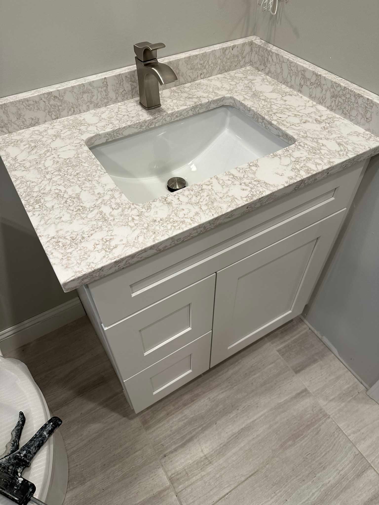 Bathroom vanity with speckled countertop, white sink, and chrome faucet on light wood floor.