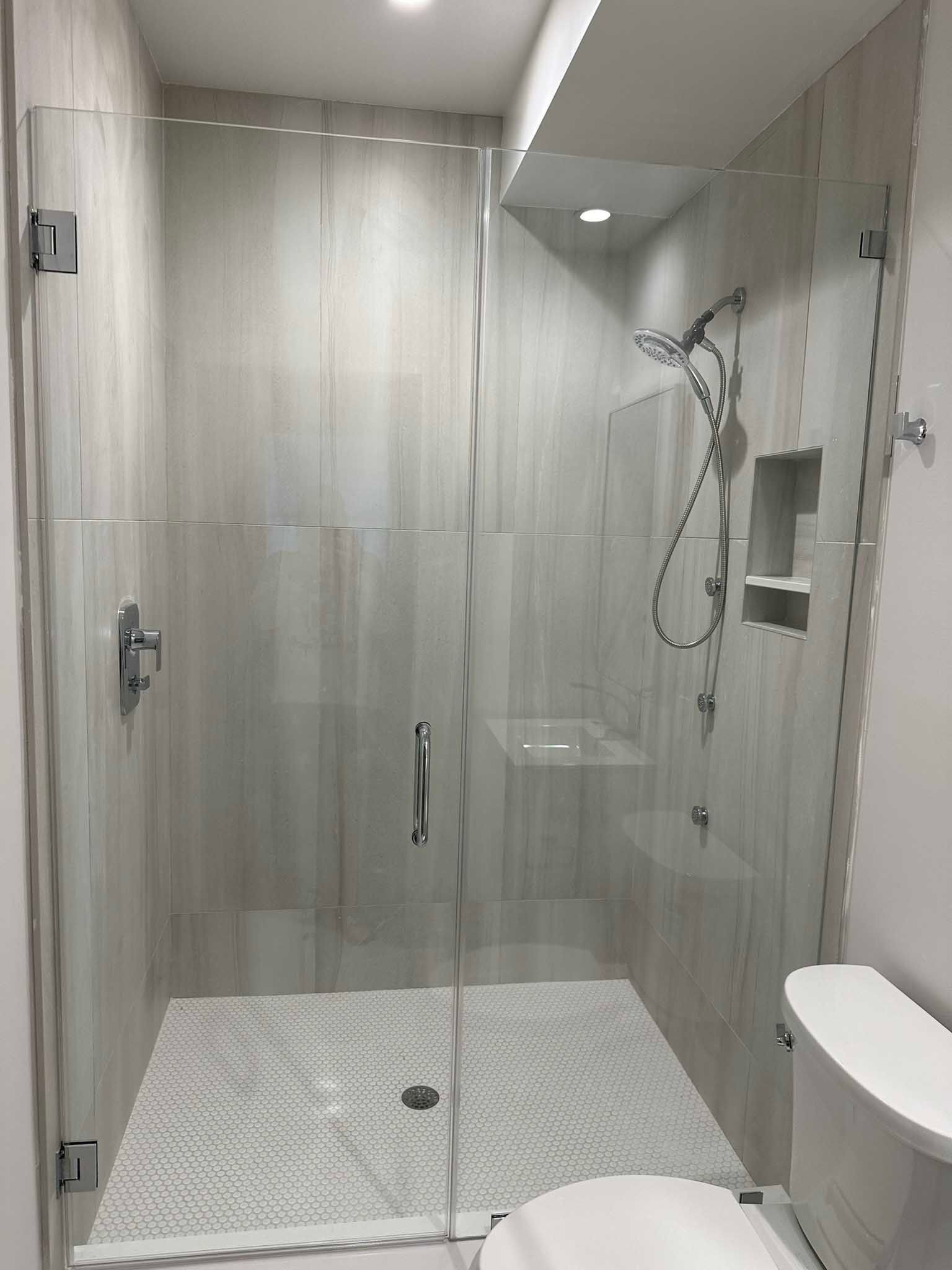 Modern bathroom shower with glass doors, white tile, and handheld showerhead