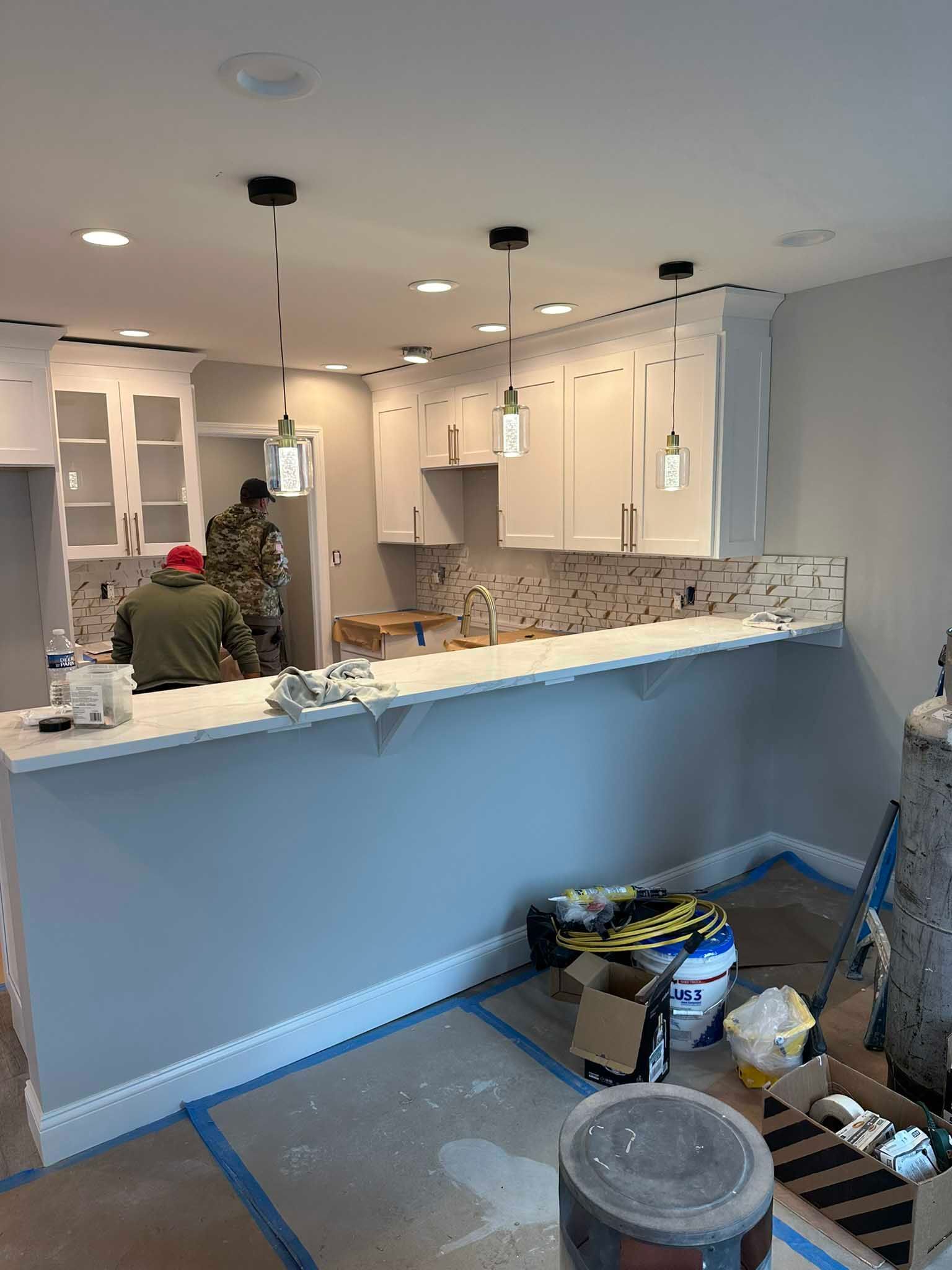 Kitchen under renovation with white cabinets, blue island counter, and tools and supplies on the floor