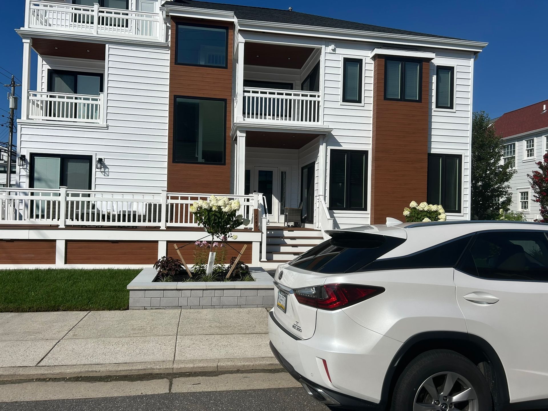 Modern two-story white house with wooden accents with a white SUV parked outside.