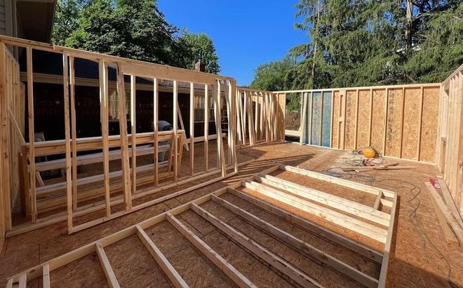 Wood-framed foundation under construction in a sunny backyard, with blue sky and trees overhead.